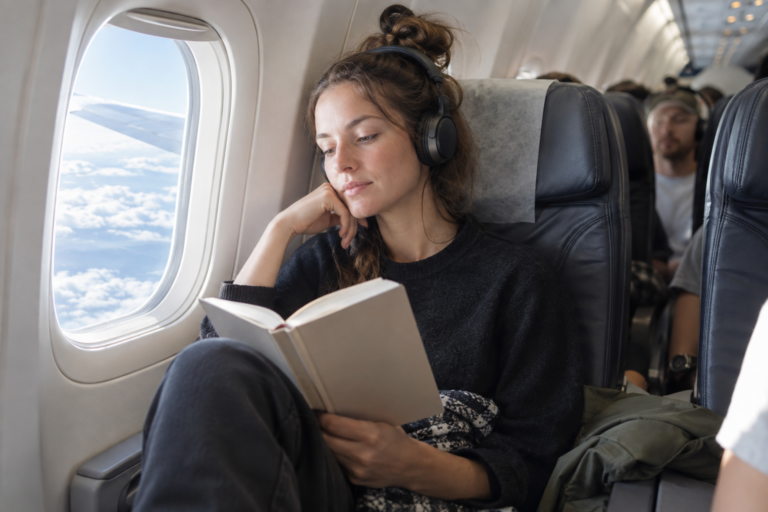 Frau liest mit Kopfhörern im Flugzeug
