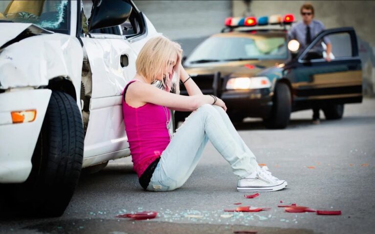 Frau sitzt nach einem Autounfall neben einem beschädigten Fahrzeug