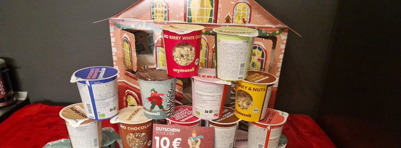 Gestapelte Bio-Müsli-Becher vor dem Weihnachtshaus mit 10-Euro-Gutschein