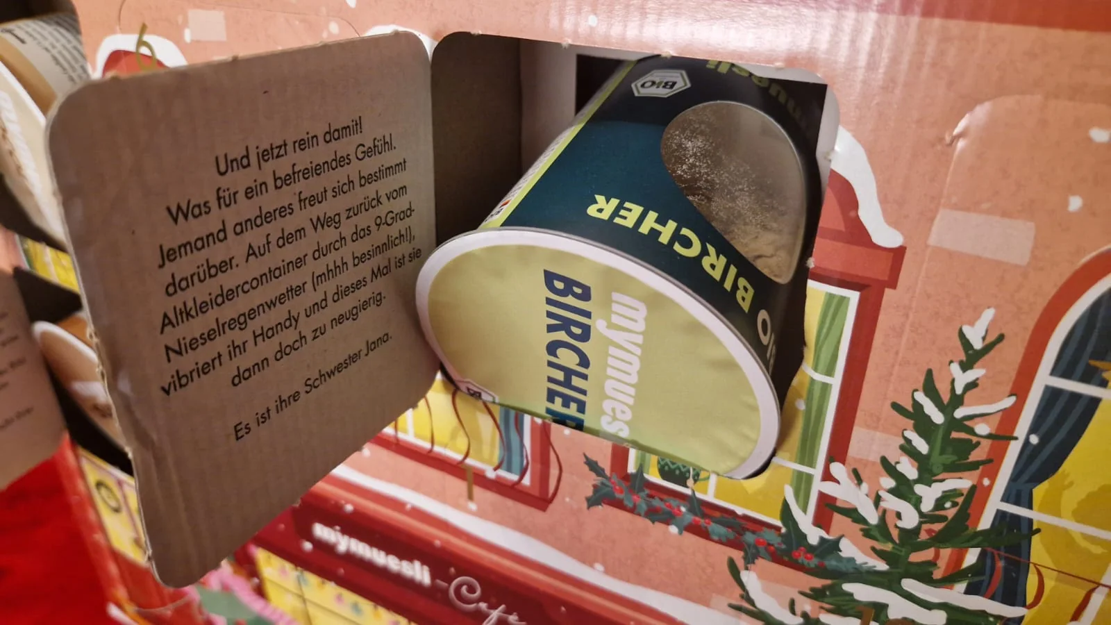 Bircher-Müsli-Becher im geöffneten Türchen mit aufgedruckter Weihnachtsgeschichte