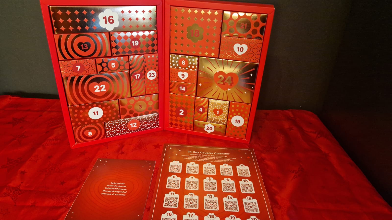 Geöffnetes rotes Kalenderbuch mit 24 nummerierten Geschenkboxen und beiliegenden Unterlagen